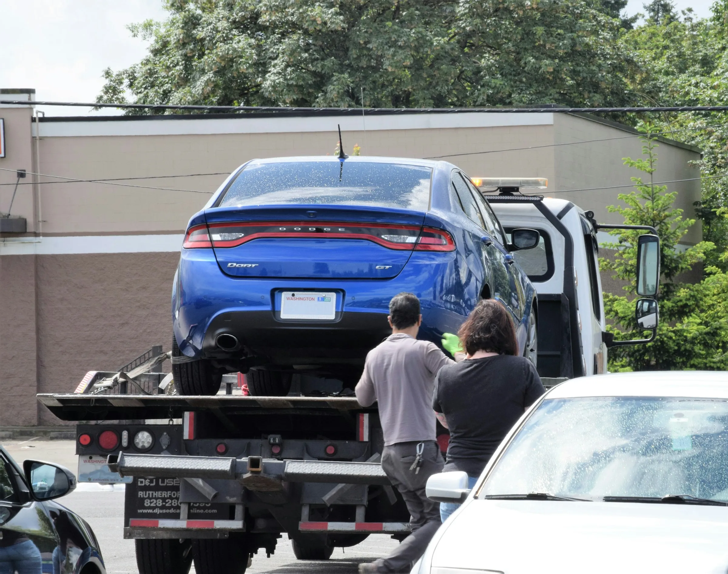 A blue sedan being loaded onto a flatbed tow truck